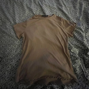 Beige ribbad topp - Säljer en beige ribbad topp med korta ärmar och vågig kant vid ärmslut och nederkant. Perfekt för en avslappnad stil.