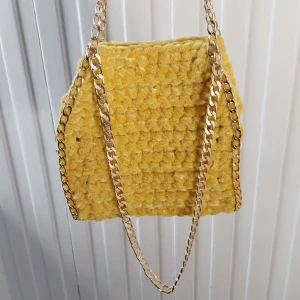 Gul virkad väska med guldkedja - Snygg gul virkad väska med en glansig guldkedja. Väskan har en unik textur och är perfekt för att ge en färgklick till din outfit. Den är både trendig och praktisk med sin rymliga design.