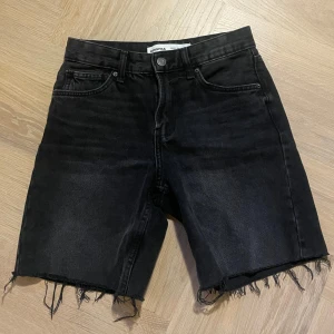 Svarta jeansshorts från Bershka - Snygga svarta långa jeansshorts från Bershka med fransiga kanter. Perfekta för en avslappnad stil. De har en klassisk femficksdesign och knappgylf.