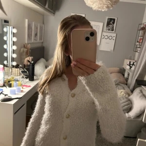 Vit fluffig kofta med knappar - Mysig vit kofta med fluffig textur och dekorativa knappar. Perfekt för kyliga dagar när du vill ha något bekvämt och stilrent. Långärmad design som ger extra värme.