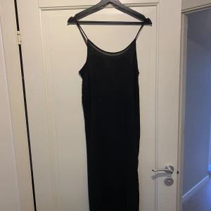 Svart långklänning med tunna axelband - Elegant svart långklänning med tunna axelband. Perfekt för en stilren look. Klänningen har en enkel design som ger en tidlös känsla.