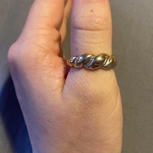 Guldfärgad ring med tvinnad design - Elegant guldfärgad ring med en unik tvinnad design. Perfekt för att ge en stilfull touch till din look. Passar bra till både vardag och speciella tillfällen. Vet inte storlek men för stor för min ganska medelstora tumme.