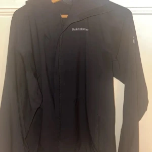 Svart vindjacka från Peak Performance - Säljer en stilren svart vindjacka från Peak Performance. Jackan har en praktisk dragkedja framtill och är långärmad. Perfekt för blåsiga dagar och har en diskret logga på bröstet.