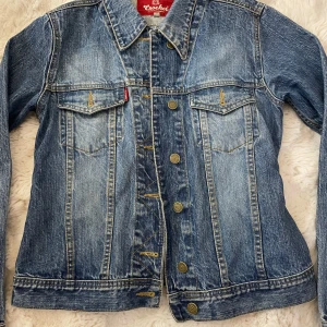 Blå jeansjacka från Crocker - Säljer en klassisk blå jeansjacka från Crocker med knappar framtill och två bröstfickor med lock. Jackan har en snygg tvättad look och långa ärmar..