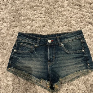 Jeansshorts från H&M Divided - Snygga lågmidjade jeansshorts från H&M i mörkblå denim med fransiga kanter. 