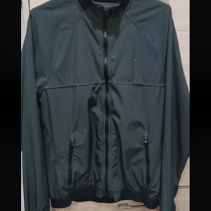 Svart jacka från Polo Ralph Lauren - Snygg svart jacka från Polo Ralph Lauren med dragkedja och broderad logga på bröstet. Jackan har långa ärmar och ribbade muddar vid ärmslut och nederkant. Perfekt för en stilren look.