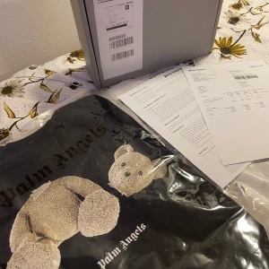 Palm angels T-shirt äkta med alla tillbehör  - Snygg svart t-shirt från Palm Angels med ett unikt nalletryck på framsidan. T-shirten har korta ärmar och är tillverkad i ett mjukt material för en bekväm passform. Perfekt för dig som vill ha en stilren men ändå lekfull look. Nypris 3000kr