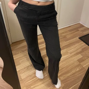 Mörkgråa kostymbyxor från H&M - Snygga gråa kostymbyxor från H&M i storlek 34. Byxorna har en klassisk rak passform med diskreta ränder och knappar bak. Lågmidjade. Passar en som är runt 170cm i längden. Jag rullade upp de lite i benen. Jag är 160cm för referens. 