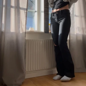 Svarta bootcut jeans - Snygga svarta bootcut jeans med låg midja och slitna detaljer vid knäna. Perfekta för en avslappnad stil. De har en klassisk femficksdesign och stängs med knappar. Köpte på hm barnavdelning storlek 164, går att justera midjan och passar mig som är 160