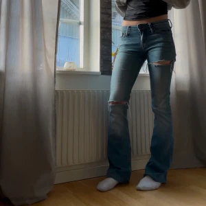 Blå bootcut jeans med slitningar - Snygga blå bootcut jeans med slitningar på knäna. De har en klassisk femficksdesign och är perfekta för en avslappnad stil. Jeansen är lågmidjade och har en bekväm passform.