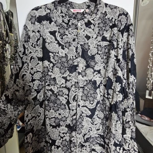 Svart och vit mönstrad blus från Indiska - Svart och vit blus med abstrakt blommigt mönster från Indiska i storlek XL. Blusen är tillverkad i 100% viskos och har långa ärmar. Den har knappar framtill uppe vid kragen och varsin knapp nere vid ärmen. Perfekt tröja för att göra en vardaglig outfit lite roligare! 😁