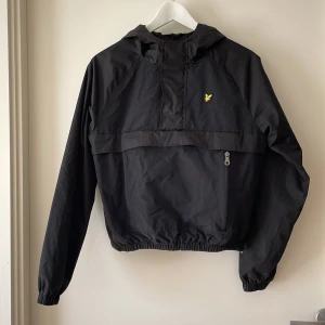Svart från Lyle & Scott - Säljer en svart jacka från Lyle & Scott i juniorstorlek 12/13 år. Jackan har en broderad gul logga på bröstet, en stor fick på magen och en dragkedja i sidan. Både dragkedja och knappar framtill i kragen. Passar bäst sommar, tidig höst och sen vår. Mycket fint skick men det är liten reva i den fodrade luvan. Djur- och rökfritt hem. 