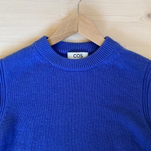 Blå stickad tröja från COS - Säljer en snygg blå stickad tröjan i karsmir från COS. Den har en klassisk rund hals och långa ärmar, perfekt för kyligare dagar. Tröjan är i mycket bra skick och passar både till vardags och lite finare tillfällen. Supermjuk och bekväm! 