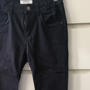 Mörkblå byxor från Lindex - Säljer ett par mörkblå byxor från Lindex i storlek EUR 164. De har en ganska smal passform. Byxorna har en knapp och dragkedja framtill samt fickor. Märket 'Detroit' syns på baksidan. Passar perfekt till höst- och vintergarderoben!