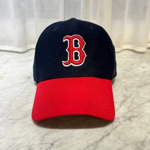 Blå och röd keps med broderad logga - Snygg keps i blått och rött från 47 Brand med en broderad 'B' logga framtill. Kepsen har en justerbar rem baktill med texten 'Red Sox'. Perfekt för sportiga tillfällen eller som en stilren accessoar.   🧢 Jag har flera kepsar till salu på min profil och lägger upp nya  regelbundet!