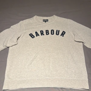 Barbour Sweatshirts  - Designad för att erbjuda en smal och samtida passform, är denna preppy tröja tillverkad av en lätt bomullsblandning och har långa ärmar och en rund hals. En kontrasterande Barbour-logotyp pryder bröstet med vintage-stil Cornelli-sömnad. Välvårdad!