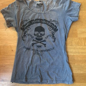 Grå t-shirt med dödskalletryck - Säljer en grå t-shirt med ett coolt dödskalletryck och texten 'Dare to be different'. T-shirten sitter tajt och är i bra skick. Den är omsydd för att sitta tajtare.🥰💝
