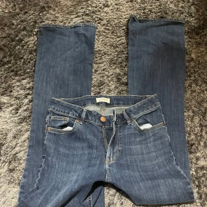Blå jeans från Lindex - Säljer ett par klassiska blå jeans från Lindex i storlek 36. De har en snygg straight passform och är perfekta för vardagsbruk. Jeansen har en traditionell femficksdesign och stängs med dragkedja och knapp. Perfekta för både höst och vår!