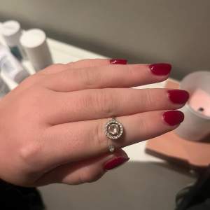 Säljer en superfin silverring med en stor glittrande sten i mitten, omgiven av mindre stenar. Ringen är justerbar och passar perfekt för både vardag och fest. Den har en modern och stilren design som verkligen fångar ögat. Perfekt för att ge lite extra bling till din outfit! 💍✨