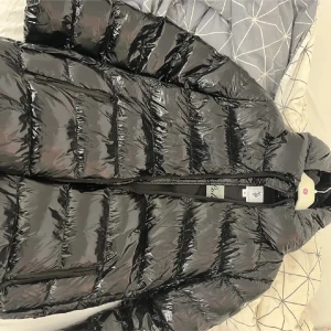 Svart glansig pufferjacka från U.S. Polo Assn. - Säljer en svart glansig pufferjacka från U.S. Polo Assn. Perfekt för kalla dagar med sin tjocka vaddering. Jackan har en hög krage och dragkedja framtill. Den är i mycket bra skick och redo för vinterns äventyr! 🖤