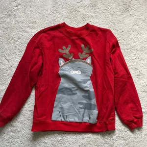 Jultröja - Superfin röd tröja från Monki med ett gulligt motiv av en katt med renhorn. Perfekt för julen! Tröjan är i bra skick och har långa ärmar. Den är gjord i mjukt material som är skönt att ha på sig. Perfekt för mysiga vinterdagar eller julfirande! 🎄