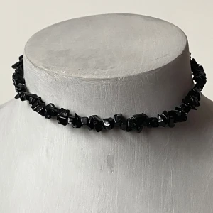 Svart choker-halsband med stenar - Snyggt svart choker-halsband med små, oregelbundna stenar som ger en cool och edgy look. Perfekt för att lyfta en outfit till fest eller vardag. Halsbandet har ett enkelt guldspänne som gör det lätt att ta på och av. Passar perfekt till både casual och mer uppklädda tillfällen.
