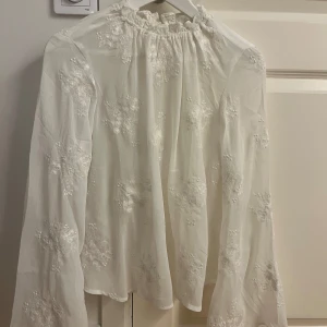 Vit blus med broderade blommor - Säljer en superfin vit blus med långa ärmar och vackra broderade blommor. Perfekt för både vardag och fest! Blusen har en lös passform och är gjord i ett lätt och luftigt material. Jättefina vida armar. OANVÄND!!
