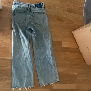 Ljusa jeans med fransiga kanter - Säljer ett par ljusa jeans med en avslappnad passform. De har en straight stil och är lite slitna vid fållen för en cool, fransig look. Perfekta för en casual outfit!