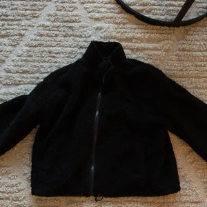 Svart teddyjacka - Mysig svart teddyjacka perfekt för kyliga dagar. Jackan har en dragkedja framtill och är långärmad. Den är supermjuk 