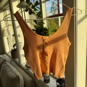 Orange ribbad linne - Säljer en ett orange/peach färgat ribbat linne med knappar framtill. Knappt använt så de är i bra skick.