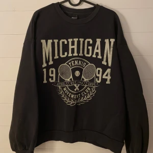 Svart sweatshirt från Gina Tricot - Säljer en svart sweatshirt från Gina Tricot med tryck 'Michigan 1994 Tennis Movement Club' i vitt. Tröjan har långa ärmar och en normal passform, perfekt för en avslappnad stil. Den är i bra skick och superbekväm att ha på sig. Perfekt för höst och vinter!