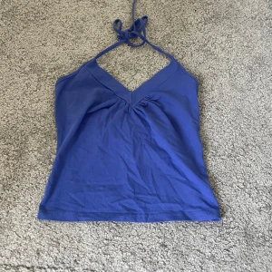 Blå halterneck-linnetopp - Säljer en snygg blå halterneck-linnetopp. Toppen har en v-ringad design och knytning i nacken. Perfekt för sommardagar eller en avslappnad festkväll. Materialet känns mjukt och bekvämt.