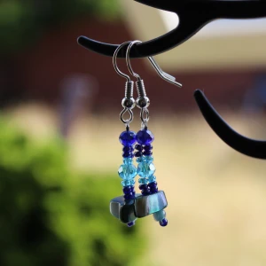 Blå och turkosa örhängen med pärlor - Säljer ett par superfina örhängen med blå och turkosa pärlor. De har en hängande design med flera pärlor i olika nyanser av blått och turkost. Perfekta för att ge en färgklick till din outfit!