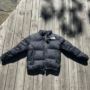 Svart dunjacka från The North Face - Säljer en svart dunjacka från The North Face i storlek XL. Jackan är perfekt för kalla vinterdagar och har en dragkedja framtill. Den är i bra skick och väldigt varm. Passar både till vardags och utomhusaktiviteter. Köp den nu och håll dig varm hela vintern! 🖤i barn storlek motsvar de XL men i dam motsvarar de XS/S/168! 