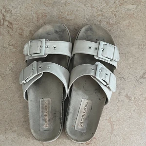 Vita sandaler från Stradivarius - Säljer ett par sandaler från Stradivarius. De har två breda remmar med stora spännen och en robust sula. Sandalerna är i välanvänt skick men fortfarande bekväma och perfekta för sommaren. behöver bara göra rent