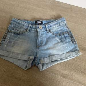 Säljer ett par snygga ljusblå jeansshorts med coola nitar på fram- och bakfickorna. De är i bra skick och har en avslappnad, lite sliten look. Perfekta för sommaren! 🩳✨