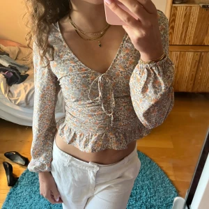 Blommig croppad blus från H&M - Säljer en superfin blommig blus från H&M i storlek S😍. Den är croppad och har långa ärmar med resår vid ärmsluten. Blusen har en söt knytning framtill och volangdetaljer vid nederkanten. Perfekt för sommar!