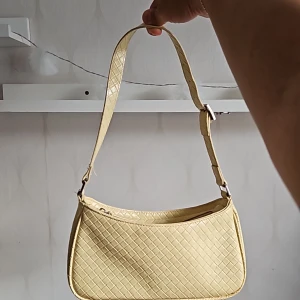 Ljusgul väska från asos - Fin ljusgul väska med ett fint mönster. Använd fåtal gångel och är i bra skick. Är liten och praktisk och kan hålla plånbok, mobil osv med mycket plats kvar.