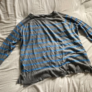 Grå och blå randig tröja - Säljer en mysig grå tröja med blå ränder. Den är långärmad och perfekt för kyligare dagar. Tröjan är i bra skick och passar till både vardag och avslappnade tillfällen. Den är mjuk och bekväm att ha på sig.