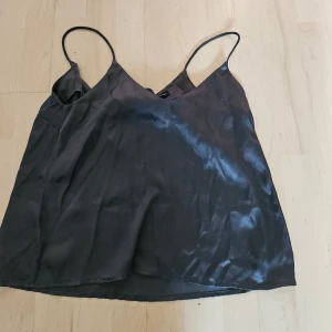 Svart satinlinne - Säljer ett snyggt svart linne i satinmaterial. Det har tunna axelband och en lös passform, perfekt för både vardag och fest. Linnet är i bra skick och känns lyxigt mot huden.