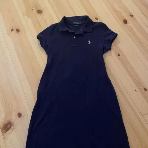 Mörkblå klänning från Ralph Lauren - Säljer en snygg mörkblå klänning från Ralph Lauren i storlek XS. Klänningen har en klassisk pikékrage och korta ärmar. Den är perfekt för både vardag och fest. Märket är broderat på bröstet i rosa. Klänningen är i bra skick och väldigt bekväm att ha på sig. Passar perfekt till sommaren eller våren!