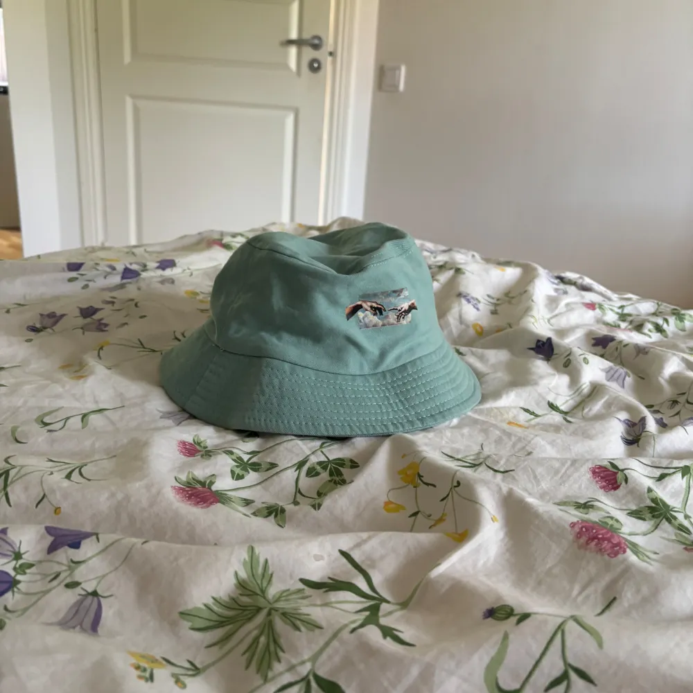 Säljer en ljusblå bucket hat med ett coolt broderi av två händer som nästan rör vid varandra. Hatten är perfekt för sommaren och har en avslappnad, normal passform. Materialet känns som bomull och är riktigt skönt att ha på sig. Perfekt för att skydda sig mot solen på stranden eller bara som en snygg accessoar till din outfit!. Accessoarer.