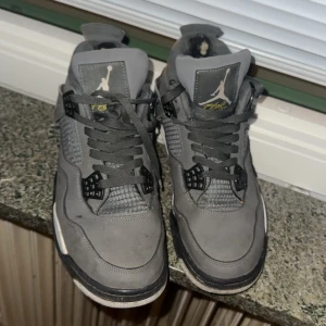 Grå Nike Air Jordan4 - Säljer ett par grå Nike Air Jordans i bra skick. Skorna har en cool design med snörning och är perfekta för både vardag och basket. De har lite slitage på insidan men är fortfarande bekväma och stiliga.