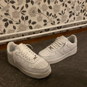 Vita Nike Air Force sneakers - Säljer ett par klassiska vita Nike Air Force sneakers. De har en stilren design med snörning och perforerade detaljer på ovansidan för ventilation. Perfekta för en casual look.