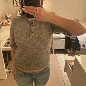 Grå stickad tröja med pärldetaljer - Säljer en grå stickad tröja med trekvartsärm och fina pärldetaljer vid halsen. Tröjan har en croppad passform som ger en modern look. Perfekt för kyligare dagar. Glittrig