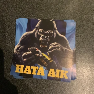 Klistermärke med gorilla och text  - Klistermärke med en aggressiv gorilla som håller en råtta, mot en blå och svart bakgrund. Texten 'HATA AIK' är tryckt i stora gula bokstäver längst ner. Perfekt för den som vill uttrycka sitt fotbollsengagemang. Finns 15 stycken 2kr styck 