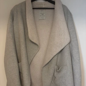 Grå teddyjacka från Bershka - Mysig grå teddyjacka från Bershka med stor krage och öppna fickor. Perfekt för kyliga dagar när du vill hålla dig varm och bekväm. Jackan har en avslappnad passform och är en del av deras premiumkollektion.