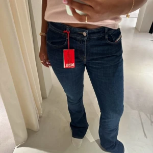 Mörkblå jeans från Diesel - Snygga mörkblå jeans från Diesel med en klassisk femficksdesign. De har en bootcut-stil och är lågmidjade, vilket ger en avslappnad och trendig look. Perfekta för en stilren vardagsoutfit.
