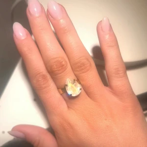 Caroline Svedbom - Elegant guldfärgad ring med en stor, droppformad klar sten. Perfekt för att ge en glittrig touch till din outfit. Aldrig använd.