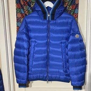 Blå dunjacka från Moncler - Snygg blå dunjacka från Moncler med dragkedja och huva. Jackan har ett quiltat mönster och Moncler-logga på ärmen. Perfekt för kyliga dagar. AVRIEUX GIUBBOTTO AVRIEUX MEDIUM JACKET Size:2/M Condition:8/10 med cartoon  Dm för mer info och bilder 